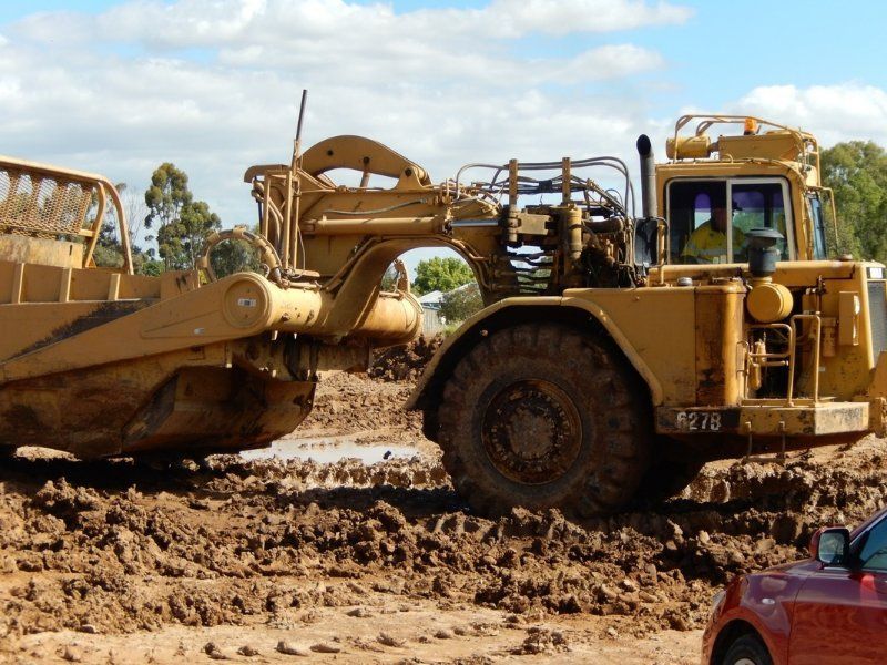 A Bulldozer is Driving Down a dirt road with trees in the Background — Mawson Constructions in Kialla, VIC