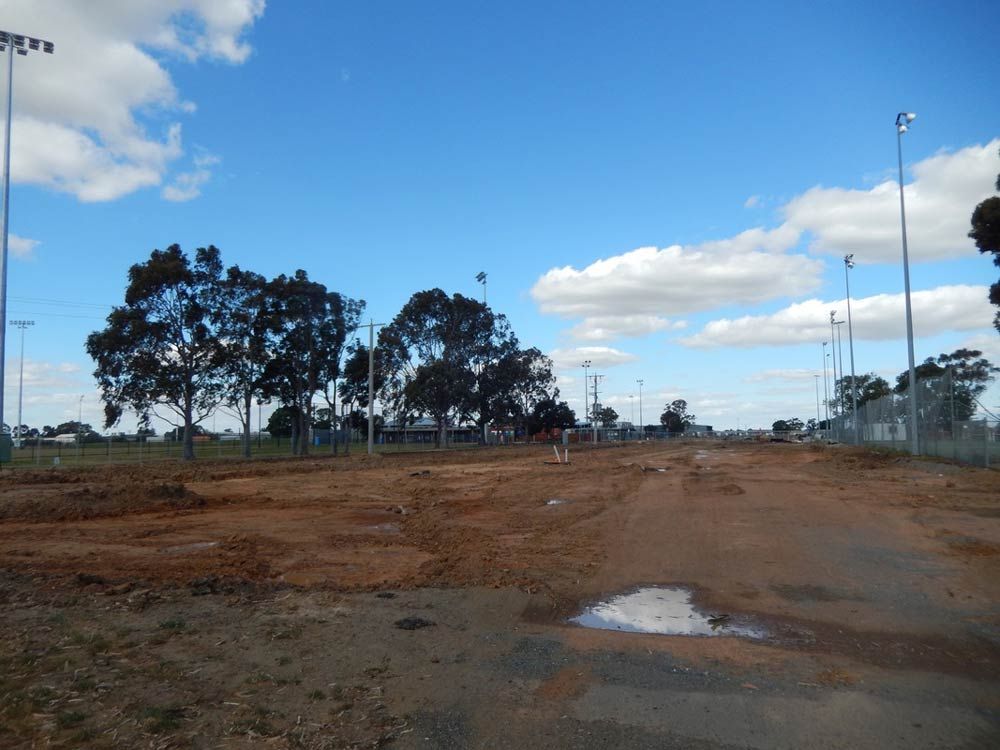 A dirt Field with Trees in the Background and a Blue sky with Clouds — Mawson Constructions in Kialla, VIC