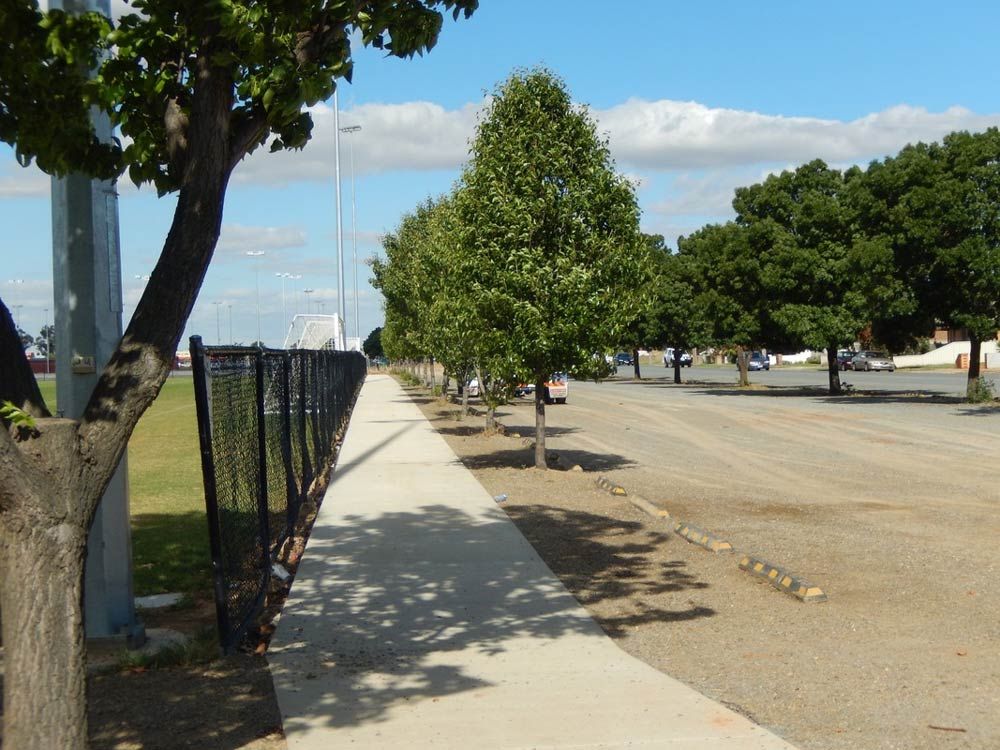 A Sidewalk Lined with Trees and a chain link fence — Mawson Constructions in Kialla, VIC