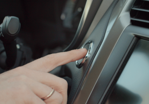Person pressing a vehicle push-button start system inside a car near the dashboard.