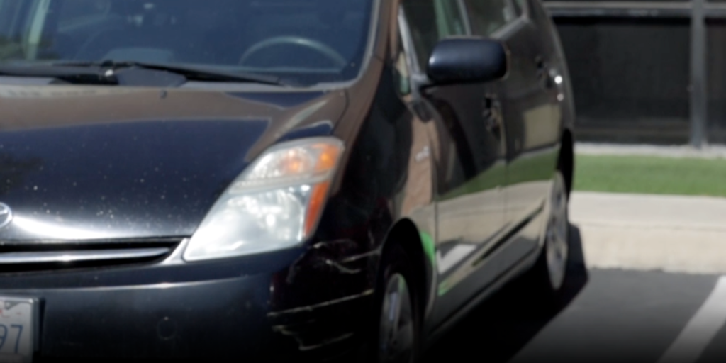 Front view of a dark-colored Prius parked in a lot near a building.
