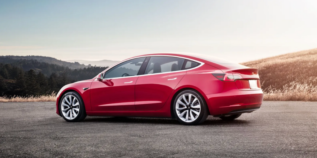 Red sedan parked on an open road with scenic hills in the background.
