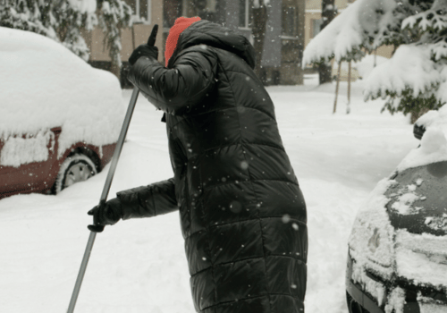 Person clearing heavy snow around parked cars in a residential area, highlighting winter weather.