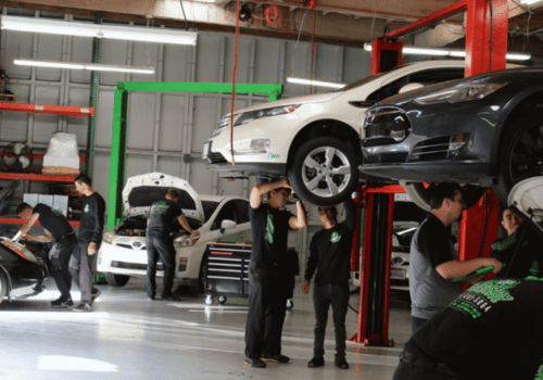 Busy auto repair shop with multiple technicians servicing vehicles on lifts, performing inspections.