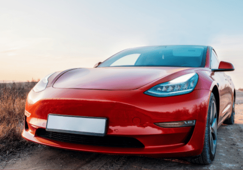 Red Tesla electric car parked on a dirt road.