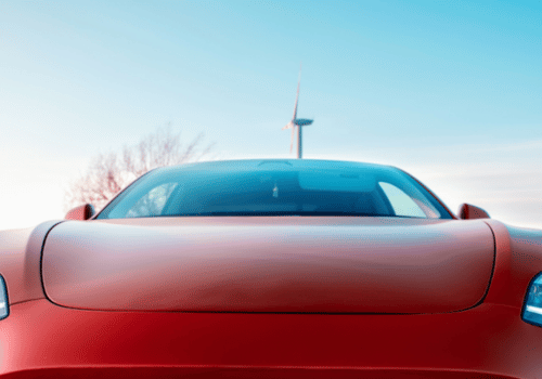 Front view of a red car with sleek headlights under a clear sky, with a wind turbine visible.