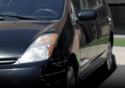 Front view of a dark-colored Prius parked in a lot near a building.