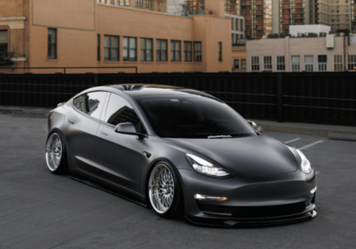 Matte black Tesla parked in an urban setting with city buildings in the background.