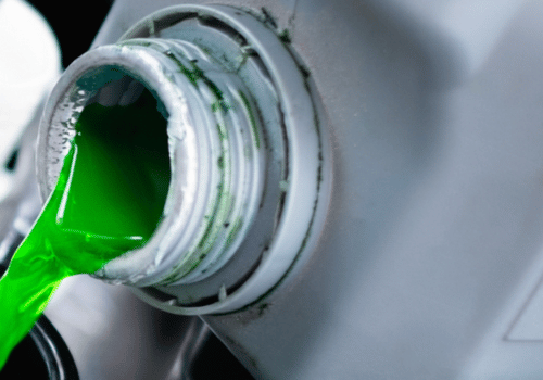 Close-up of bright green coolant being poured from a container, showing automotive fluid maintenance