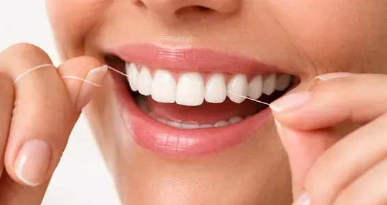 Une personne qui sourit en utilisant du fil dentaire entre ses incisives supérieures.