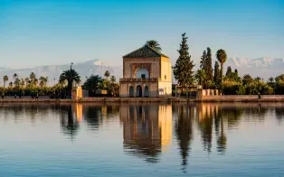 Le pavillon des jardins de la Ménara se reflétant dans un grand bassin, avec des palmiers et les sommets.