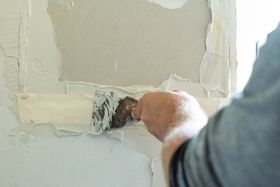 A person uses a putty knife to scrape plaster from a wall during ремонт.