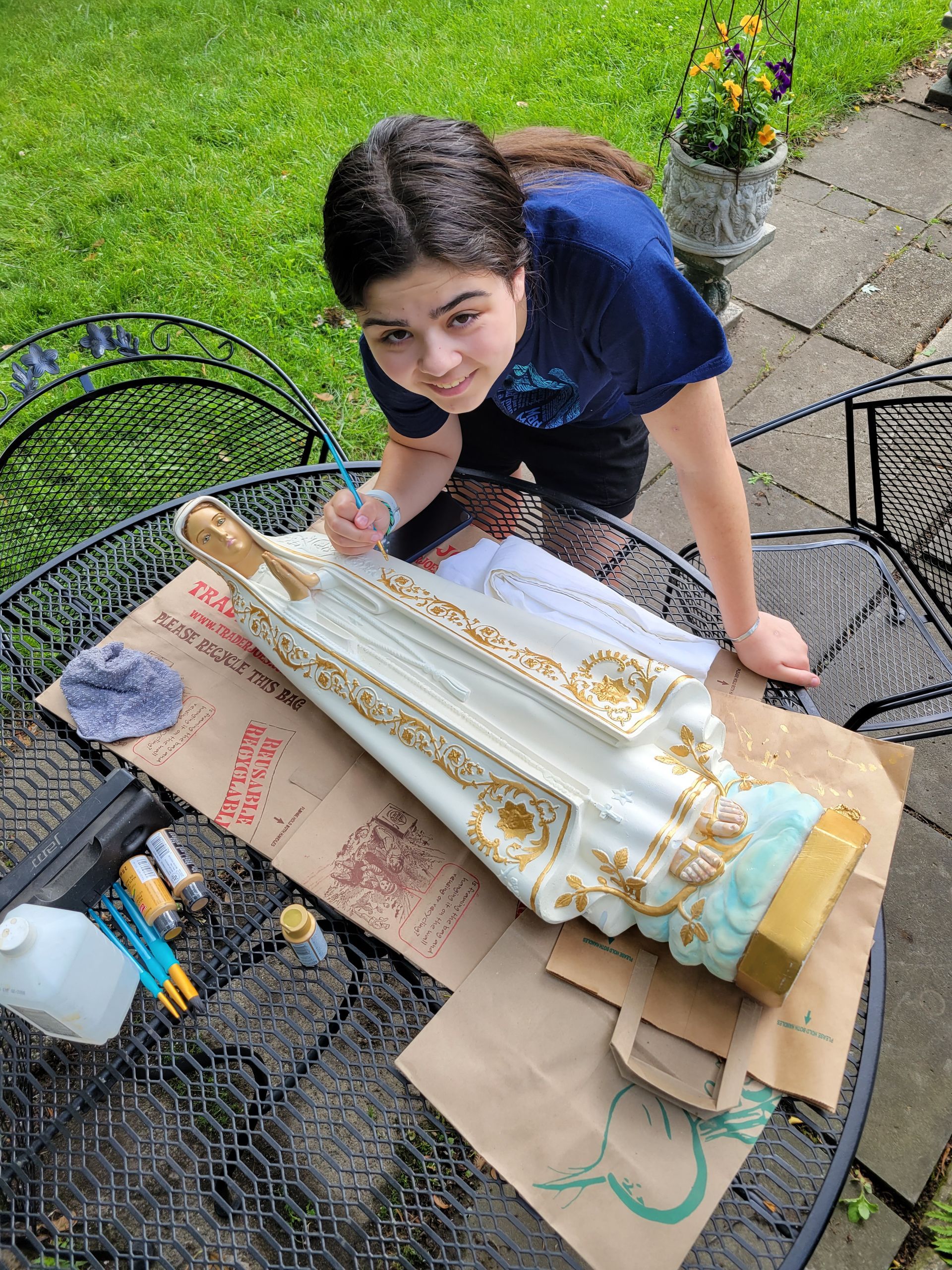A young girl is painting a statue of mary on a table.