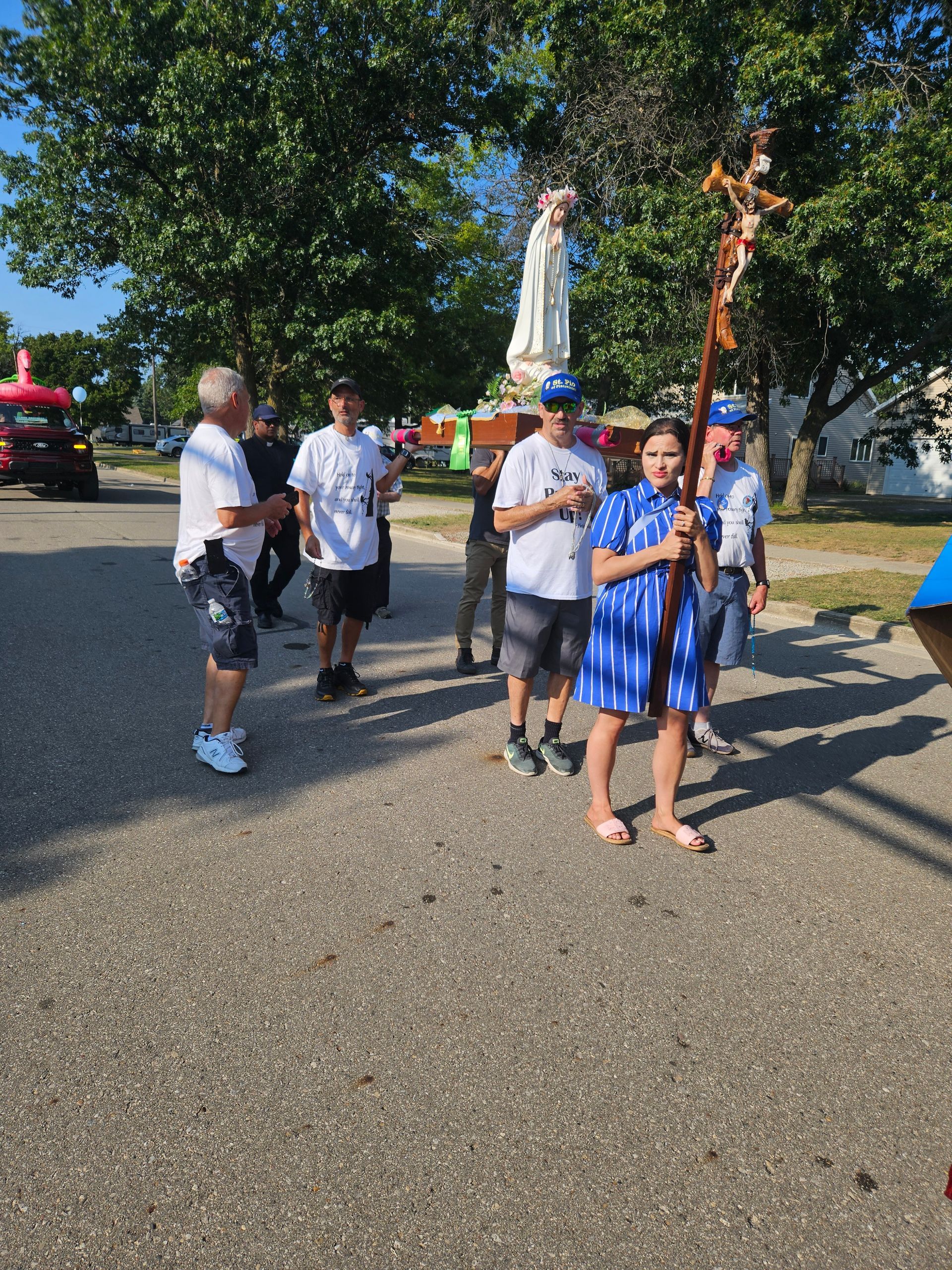 A group of people are walking down a street with a statue in the background.