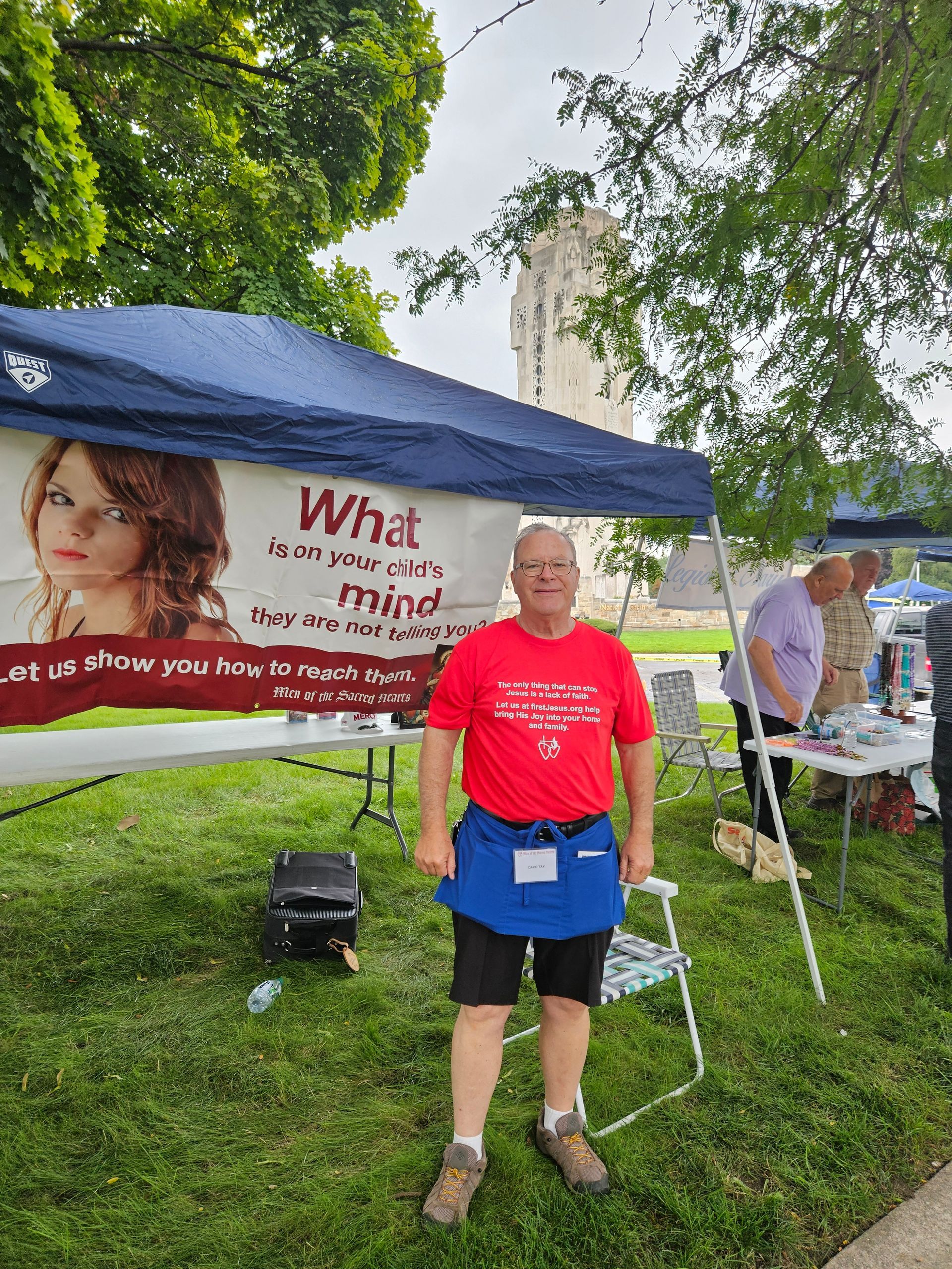 A man in a red shirt is standing in front of a tent.