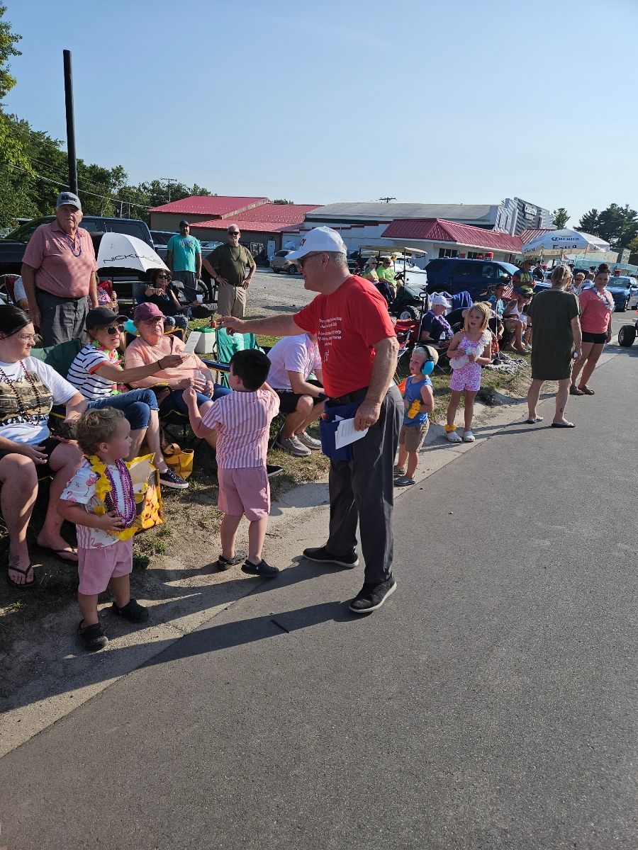A man in a red shirt is standing in front of a crowd of people at the cheeseburger festival