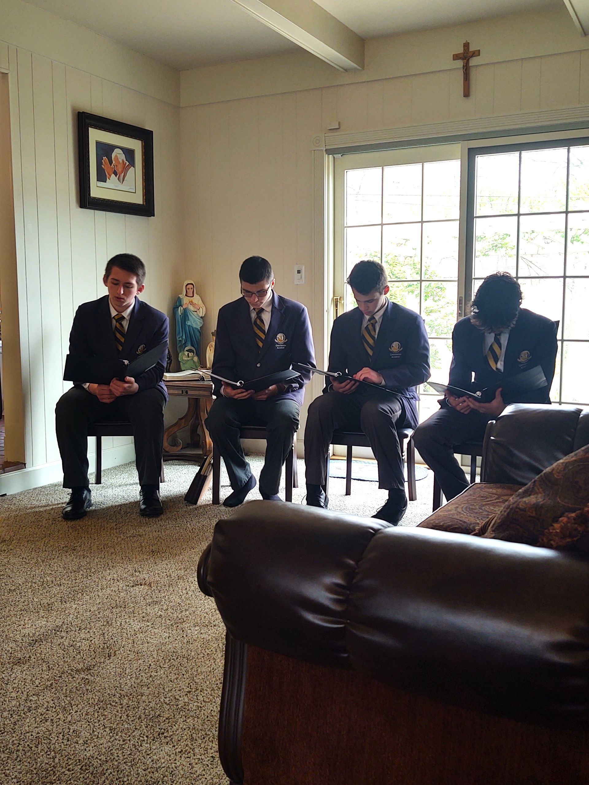 A group of young men are sitting in a living room with a cross on the wall
