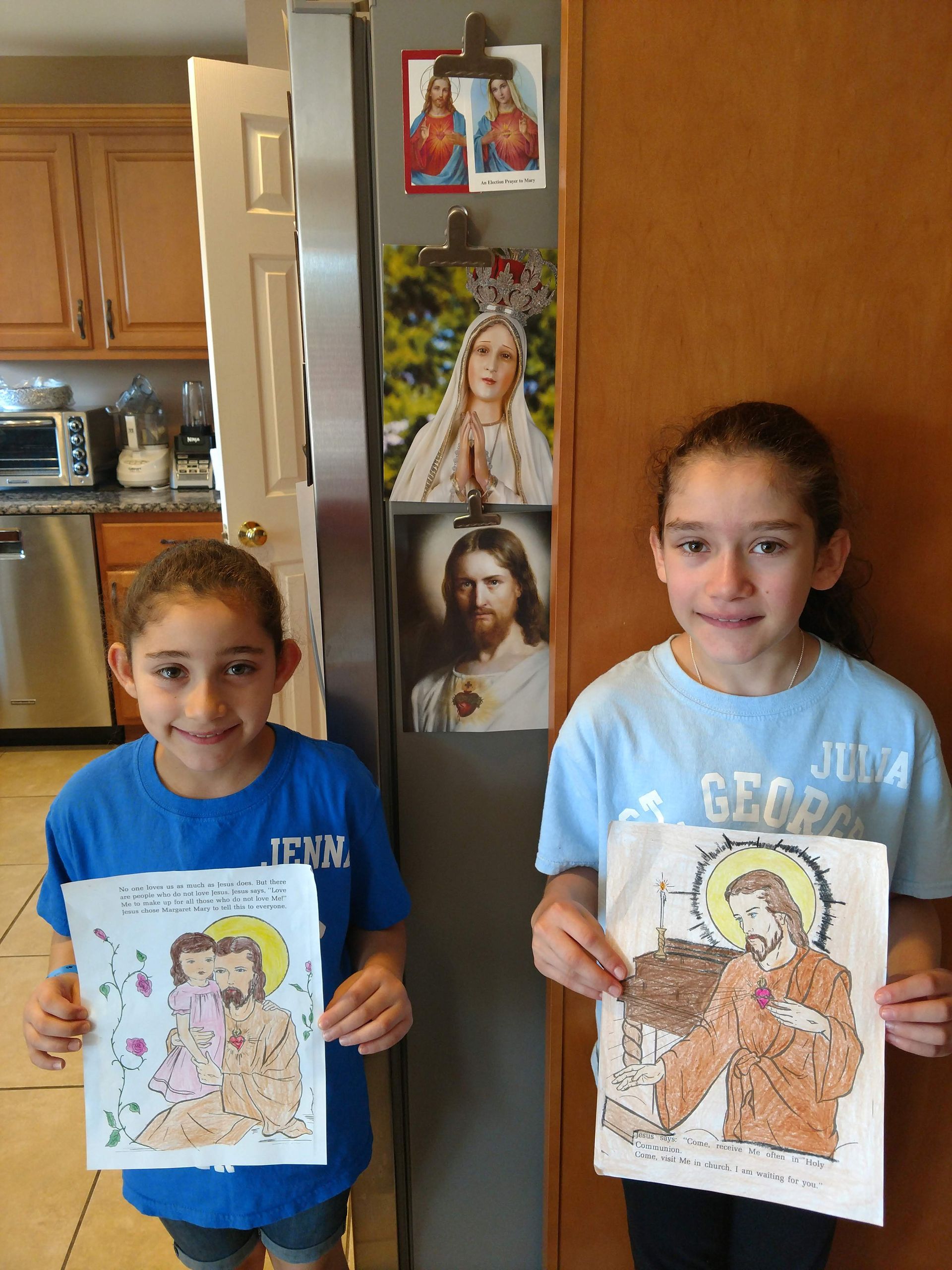 Two young girls are holding up their drawings of jesus and mary