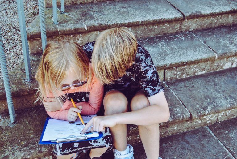 A boy and a girl are sitting on a set of stairs looking at a clipboard.