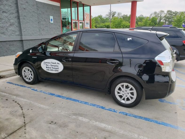 Black Toyota Prius parked near a building with tinted windows. A white decal on the side.