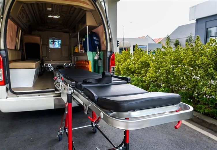 Ambulance van with back doors open, stretcher extended, medical setting, daylight.