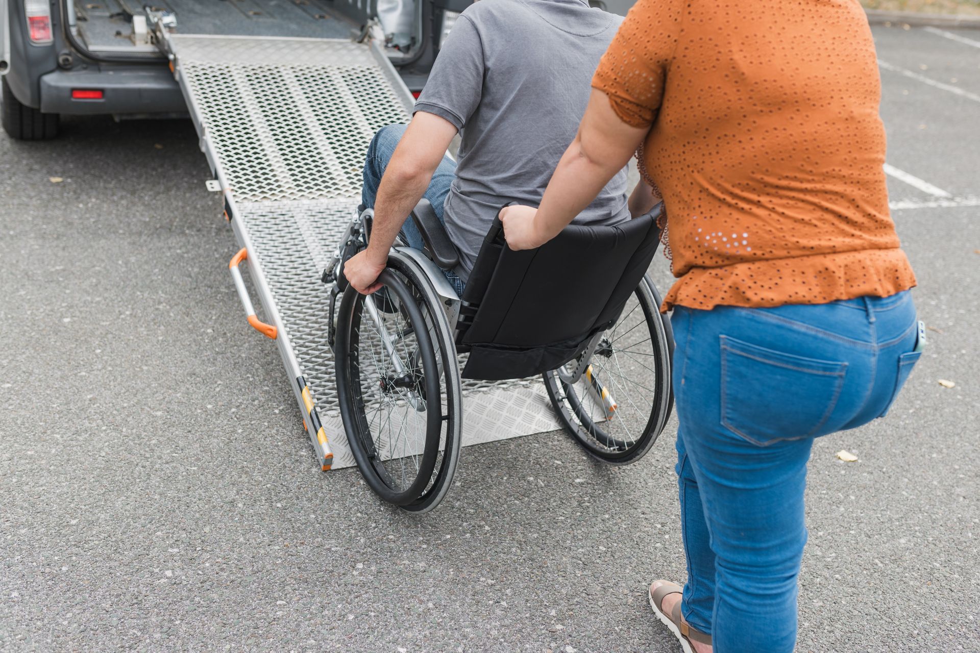 Person pushing wheelchair up ramp into van; outdoors.