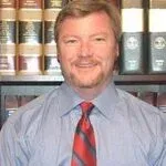 Man wearing a blue shirt and red tie, smiling in front of bookshelves.