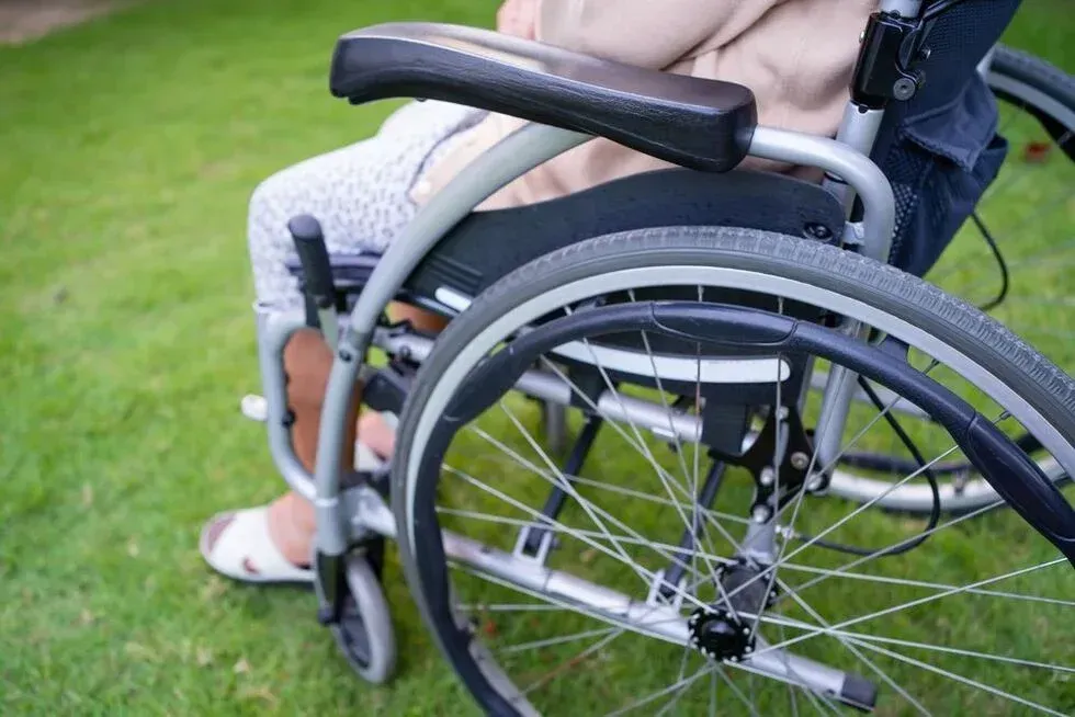 Person in a wheelchair on grass, view of the wheelchair and a leg, wearing sandals.