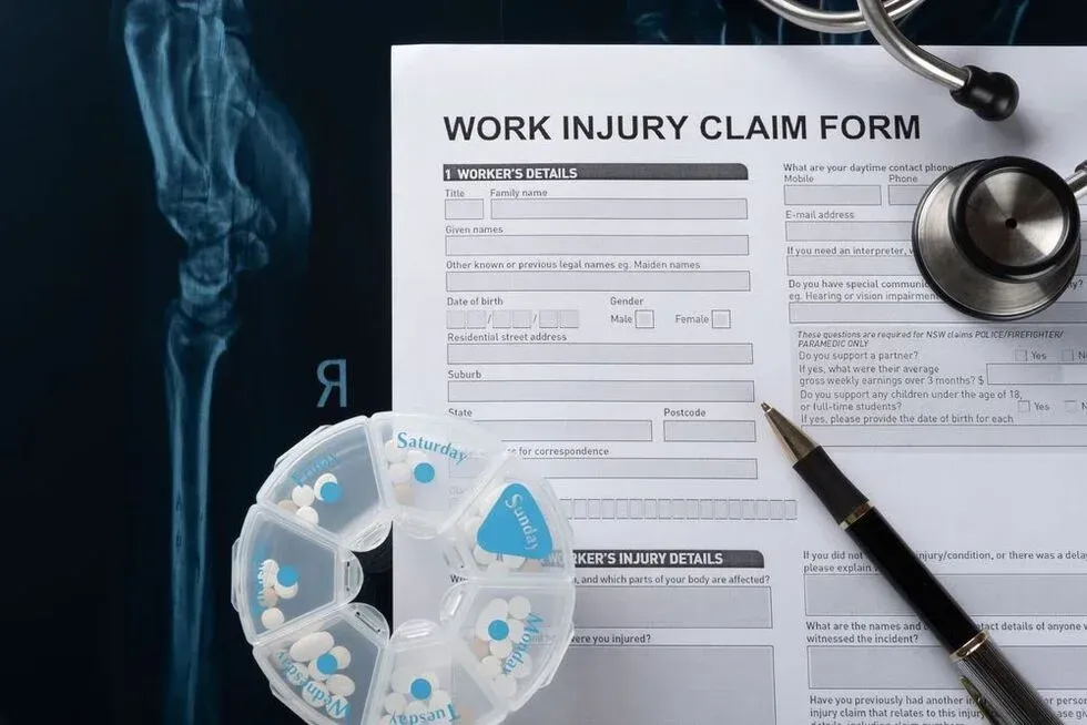 Work injury claim form with pen, stethoscope, pills, and X-ray of an arm.