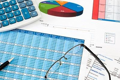 Calculator, pie chart, financial spreadsheets, and eyeglasses on a desk.