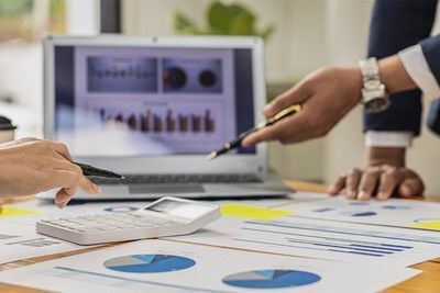 People reviewing financial data on a laptop and printed charts, using pens and a calculator.