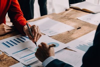 Hands pointing at charts and graphs on a wooden table during a business meeting.