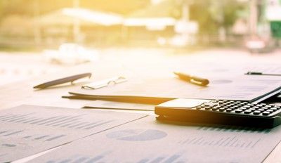Calculator, pens, and eyeglasses on papers with charts, outdoor background, sunny.