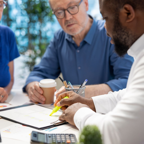 Three people reviewing documents at a table. One person highlights text with a yellow marker.