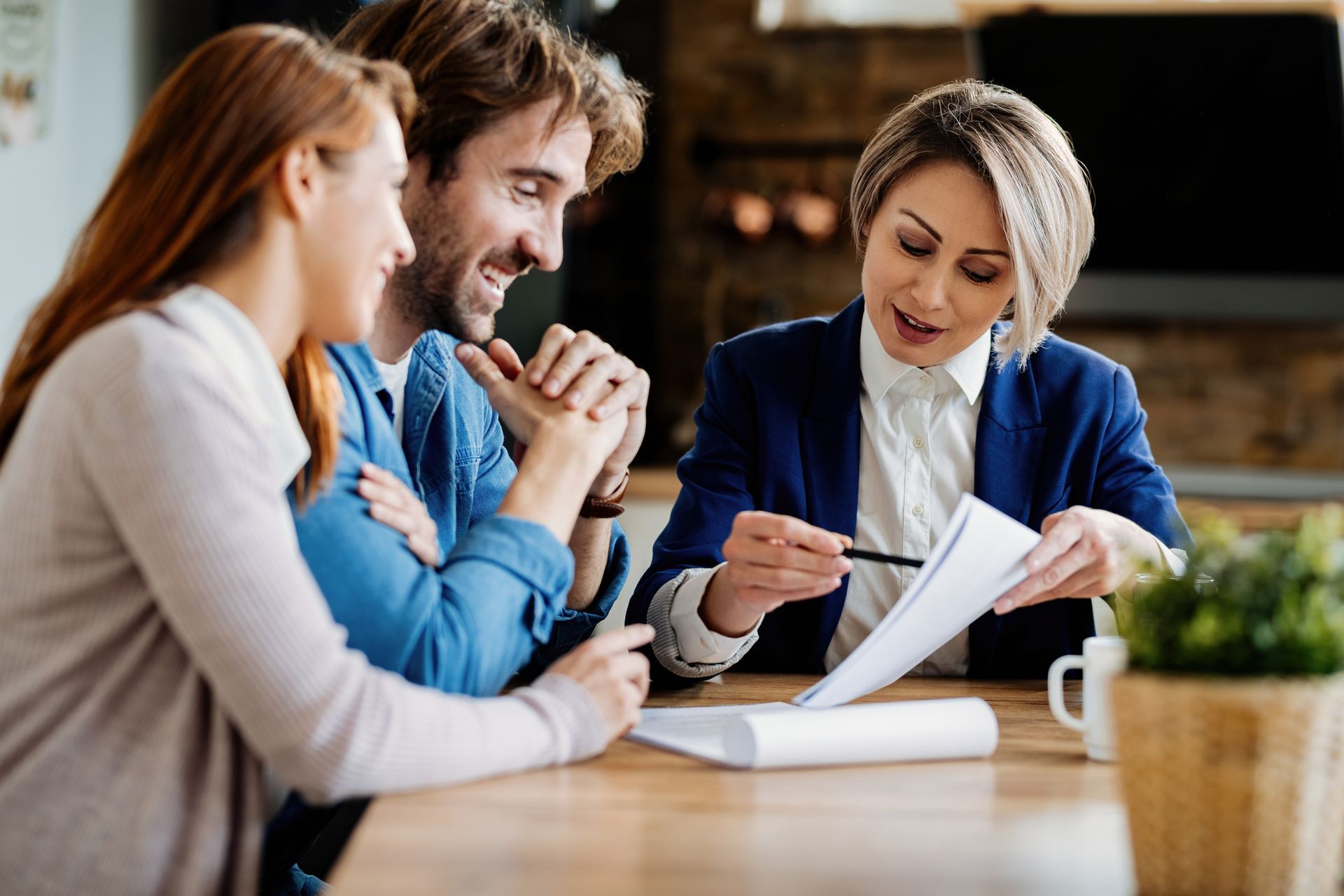 Woman in blazer reviews paperwork with a couple at a table.