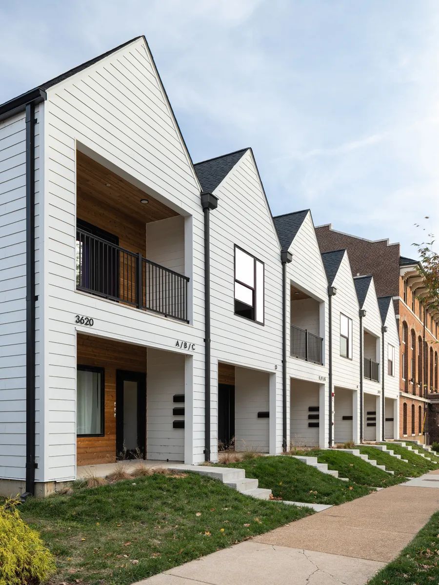 A row of white houses with balconies and a sidewalk in front of them.