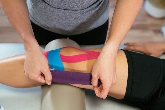 Manos de una fisioterapeuta femenina que pone cinta médica en la rodilla de un paciente