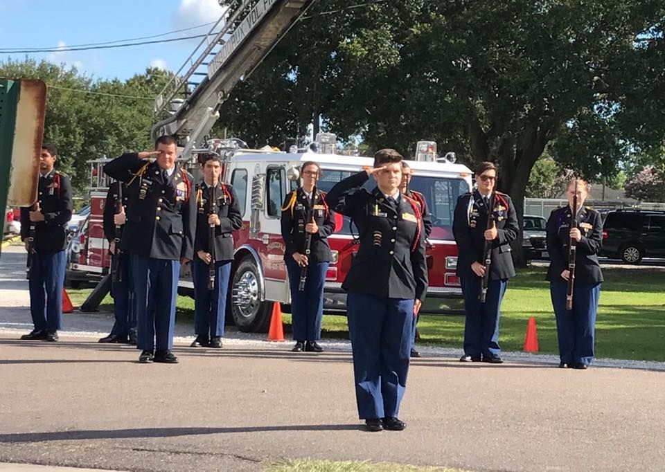 A group of soldiers salute in front of a fire truck
