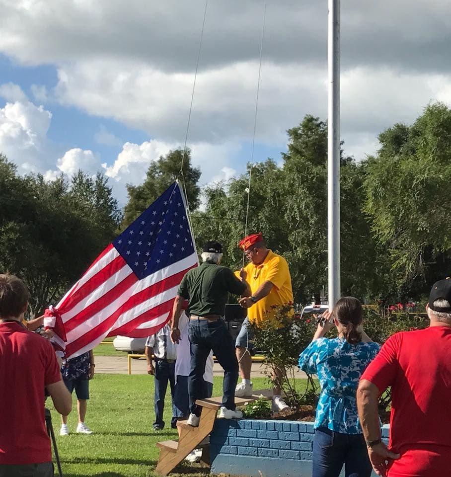 A group of people standing around a flag pole holding an american flag
