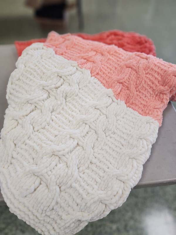 A close up of a pink and white knitted scarf on a table.