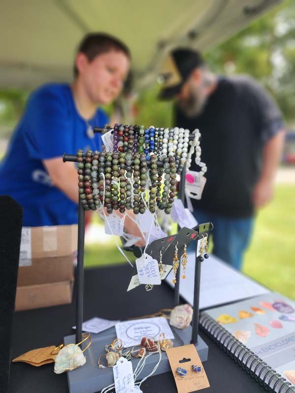 A man is standing behind a table with a display of bracelets and earrings.