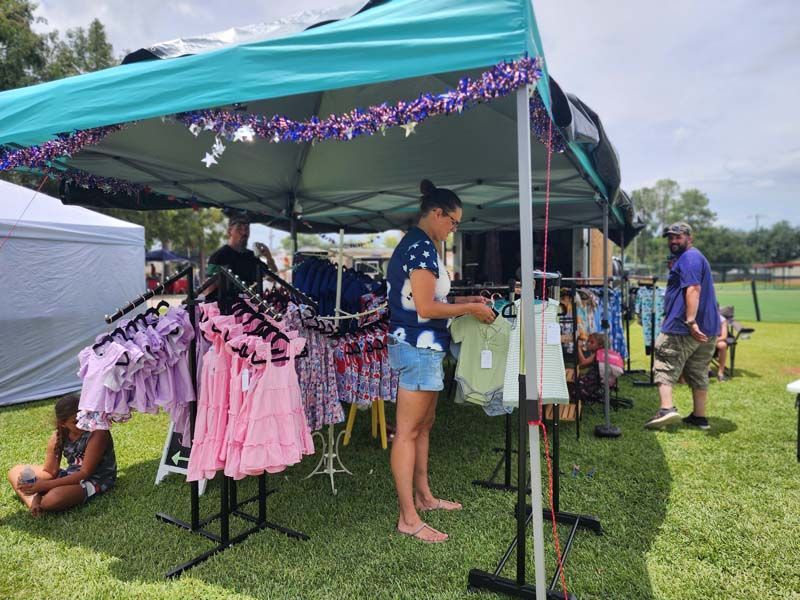 A woman is standing under a tent looking at clothes.