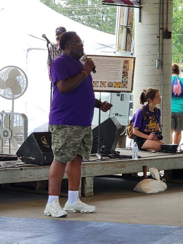 A man in a purple shirt is speaking into a microphone