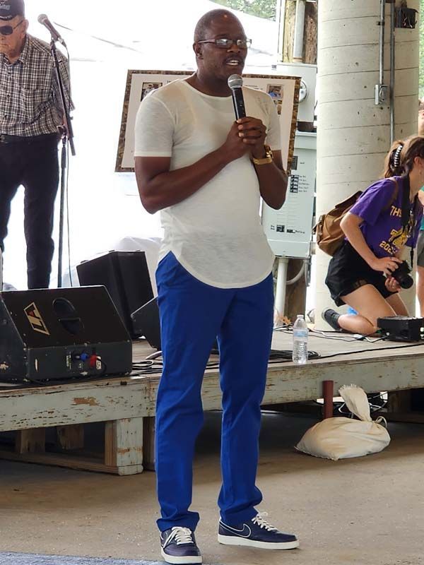 A man in a white shirt and blue pants is speaking into a microphone