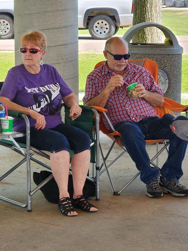 A man and a woman are sitting in folding chairs eating ice cream