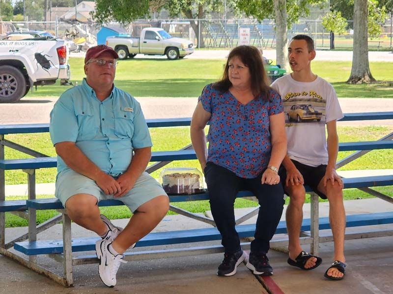 Three people are sitting on a picnic table in a park.