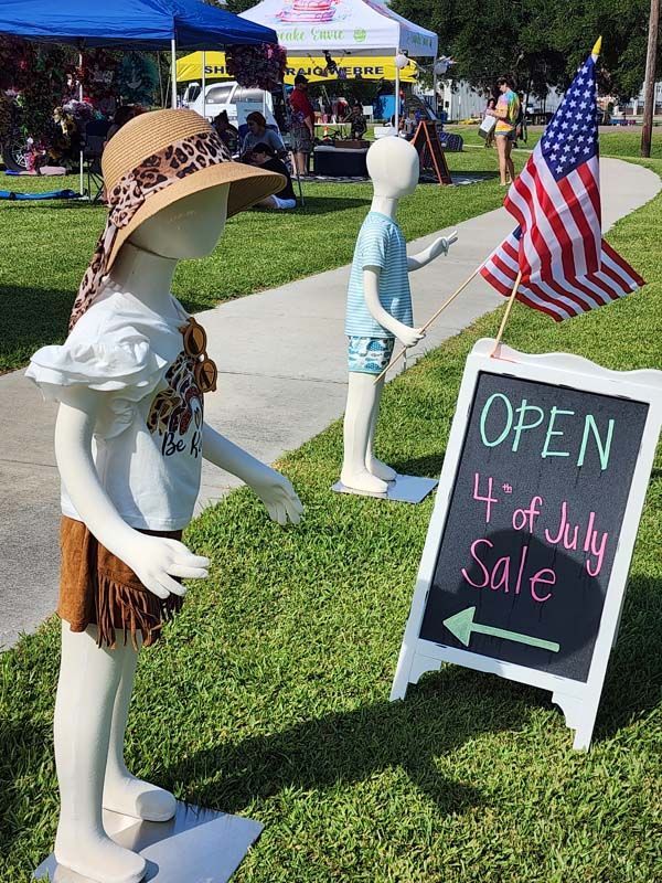 Two mannequins are standing next to a sign that says open 4th of july sale