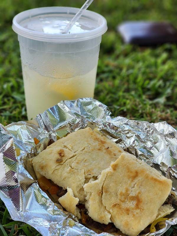 A sandwich is wrapped in tin foil next to a cup of lemonade.