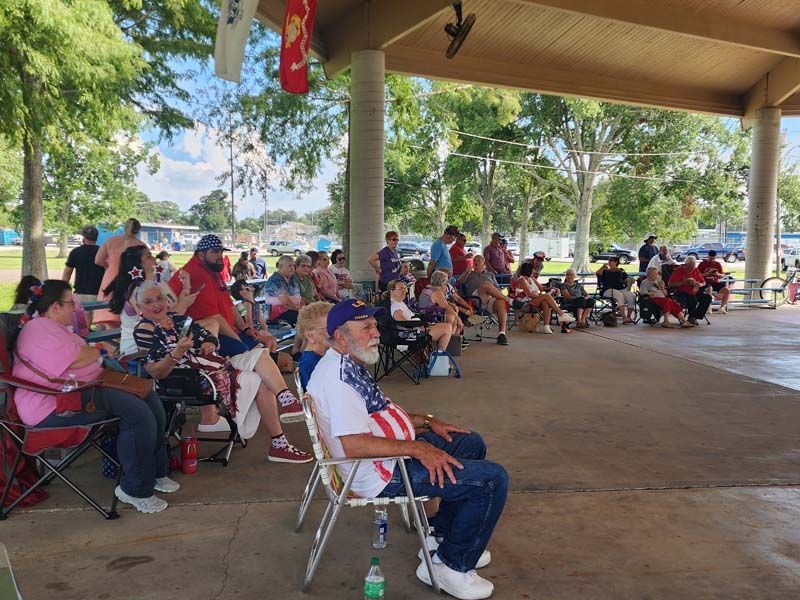 A group of people are sitting in chairs under a covered area.
