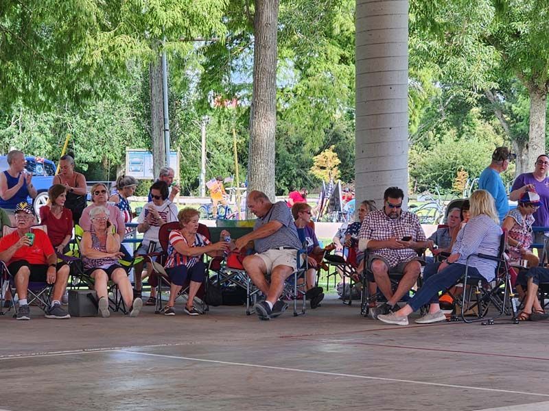 A group of people are sitting in chairs under a canopy in a park.
